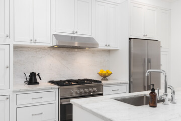 Wall Mural - A kitchen detail with white cabinets, stainless steel stove and hood, marble countertops and backsplash, and a chrome faucet.