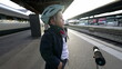 One pensive young boy standing at train platform wearing helmet staring blankly into the horizon daydreaming. Thoughtful Child with hands in pocket waiting for transportation to arrive