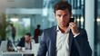 © Tahir - A young businessman who is upset is talking on the phone while in front of an office background.