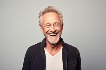 Portrait of a happy senior man laughing while standing against grey background.