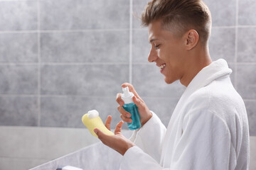 Sticker - Happy young man applying face cleanser on sponge in bathroom. Space for text