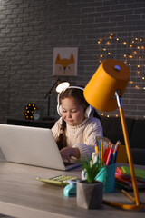 Wall Mural - Little girl with laptop doing lessons at home late in evening