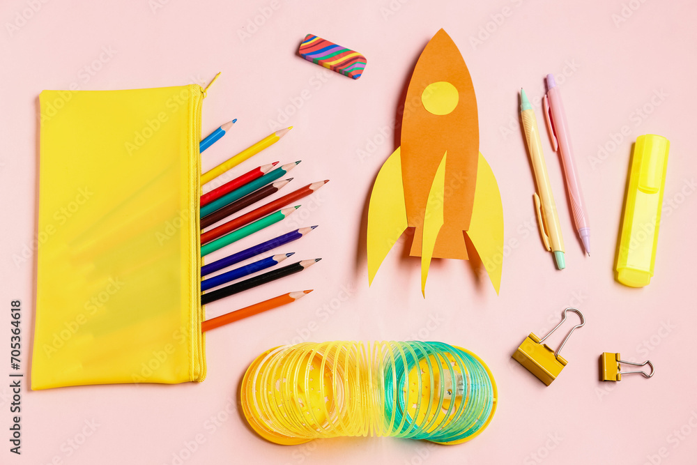 Paper rocket with pencil case and different stationery on pink background