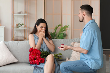 Wall Mural - Young man proposing to his girlfriend with flowers at home