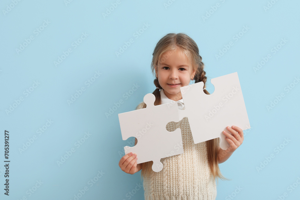 Happy little girl with puzzle pieces on blue background