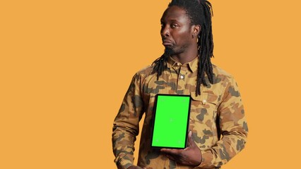 Wall Mural - African american adult with greenscreen on gadget, presenting isolated chromakey display and smiling in front of camera. Young adult holding mobile device with copyspace blank layout.