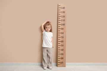 Wall Mural - Cute little girl measuring height near beige wall