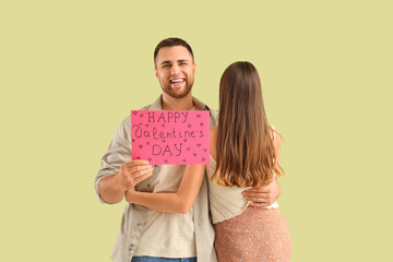 Wall Mural - Lovely couple holding greeting card with text HAPPY VALENTINE'S DAY on green background