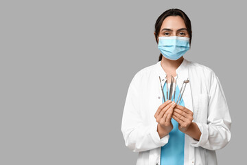 Wall Mural - Young female dentist in mask with dental tools on grey background