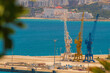 Harbour cranes against the background of the blue sea with slightly blurred contours due to the heat and warm air currents in the air. Concept of cargo transportation by sea