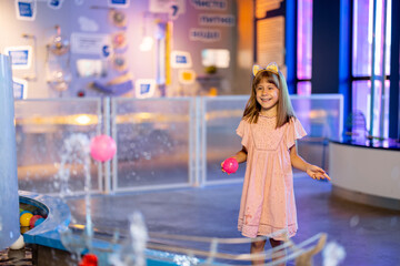 Wall Mural - Little girl plays with a ball on a steam of water, learning physical phenomena in an interesting way, having fun in a science museum with interactive models
