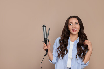 Wall Mural - Happy woman with curling hair iron on beige background. Space for text