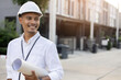 © chinnarach - close up indian engineer man smile and hold blueprint of building project in front of site for civil and construction concept
