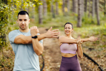 Wall Mural - Selective focus on a sportswoman stretching arms in nature with her partner.