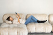 © F8  \ Suport Ukraine - Close up of a woman using a smart phone lying on a sofa in the living room at home with a cozy background