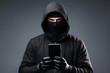 © Michael - Male criminal hacker in black clothes and balaclava with phone in hand, phone scam concept