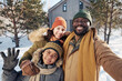 © pressmaster - Happy young family of three taking selfie and looking at camera while standing against their country house or cottage on winter day