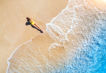 Sticker - Aerial view of the beautiful young lying woman on the tropical sandy beach near sea with waves at sunset. Summer vacation in Lefkada island, Greece. Top view of slim girl, clear azure water. Seaside