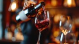 Close up female hand pouring red wine to glass. Wine expert, sommelier tasting, rating and drinking wine, bottles in background. Restaurant, wine bar, waitress. 