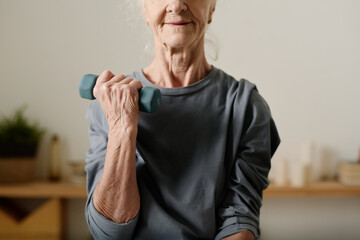 Wall Mural - Cropped shot of senior active woman in grey cotton pullover sitting in front of camera at home and practicing exercise with dumbbells