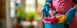 Cleaning lady holding a bucket of cleaning products in her hands on a blurred background.