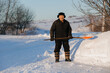 © Parilov - Elderly man cleaning snow with shovel in village after snowstorm, pensioner works as janitor