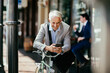 © Marko Geber - Senior businessman using smartphone during bike commute in city