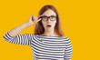 Young student girl very surprised by something. Beautiful nerdy young woman in striped top and glasses isolated on yellow background looking at camera with funny, shocked, astonished face expression