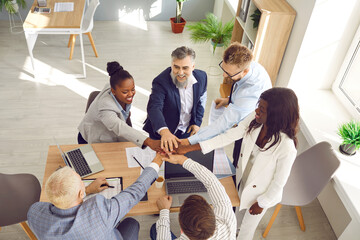 Motivated business people putting their hands together, view from above. Office team holding pile of hands engaging in team building activity, collaboration. Unity and successful teamwork