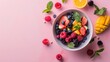  a bowl of fresh fruit on a pink surface with mint leaves and sliced oranges and raspberries on the side.