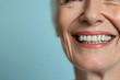 Smiling elderly person with smooth white teeth implants. Close up portrait of female mouth on pastel blue background, banner with copy space. Positive senior woman