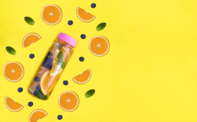 Wall Mural - Infused or detox water with orange and blueberry in the bottle on the yellow background. Copy space. Top view.