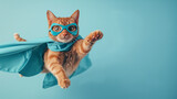 Fototapeta Zwierzęta - superhero cat, Cute orange tabby kitty with a blue cloak and mask jumping and flying on light blue background with copy space. The concept of a superhero, super cat, leader, funny animal studio shot.