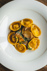 Wall Mural - Appetizing ravioli with mushrooms in a large white plate on a wooden background.