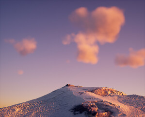 Wall Mural - Mountain covered in snow under a sky with some clouds during sunset.