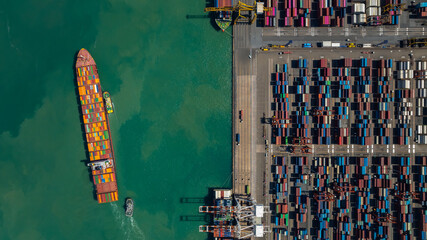 commercial port loading and unloading cargo from container ship import and export by crane for distributing goods by trailers transported to customers and dealers, aerial top view