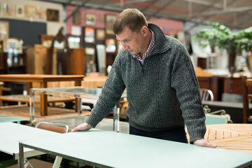 Wall Mural - Portrait of focused adult man looking for dining table in furnishings store