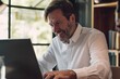 © Adriana - Smiling mature adult business man executive sitting at desk using laptop. Happy busy professional mid aged businessman ceo manager working on computer corporate technology in office
