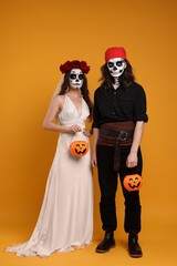 Poster - Couple in scary bride and pirate costumes with pumpkin buckets on orange background. Halloween celebration