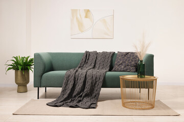 Wall Mural - Stylish living room interior with comfortable sofa, blanket, houseplant and side table