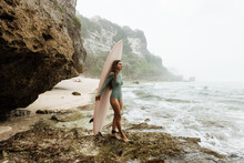 Woman surfer with surfboard going to surf at seaside. Girl holding surfboard and look for the waves