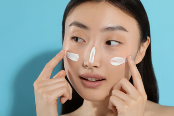 Wall Mural - Beautiful young woman with sun protection cream on her face against light blue background. Space for text