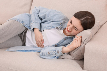 Wall Mural - Young woman suffering from stomach pain on sofa