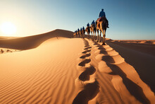 A Caravan Of Camels Forms A Line As It Treks Across The Golden Sand Dunes Of The Desert Under The Warm Glow Of The Setting Sun.
