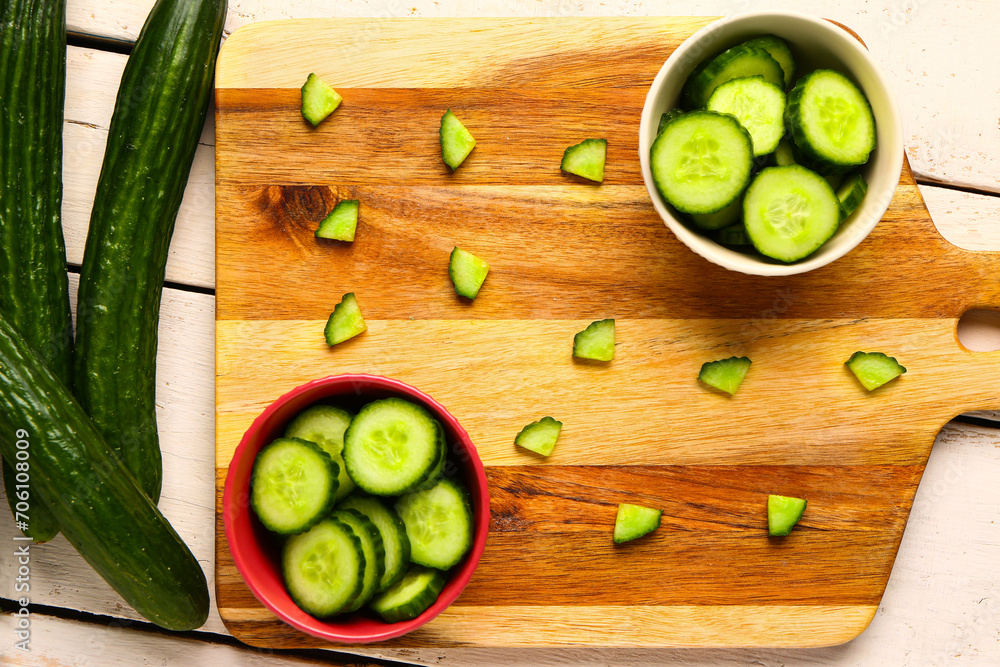 Bowls with fresh cut cucumber on light wooden background