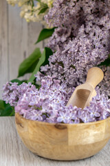 Wooden Bowl with wooden spoon of fresh purple lilac petals with branch of blooming lilac. Lilac flowers fragrance. Concept for spa wellness and aromatherapy. Copy space Still life composition