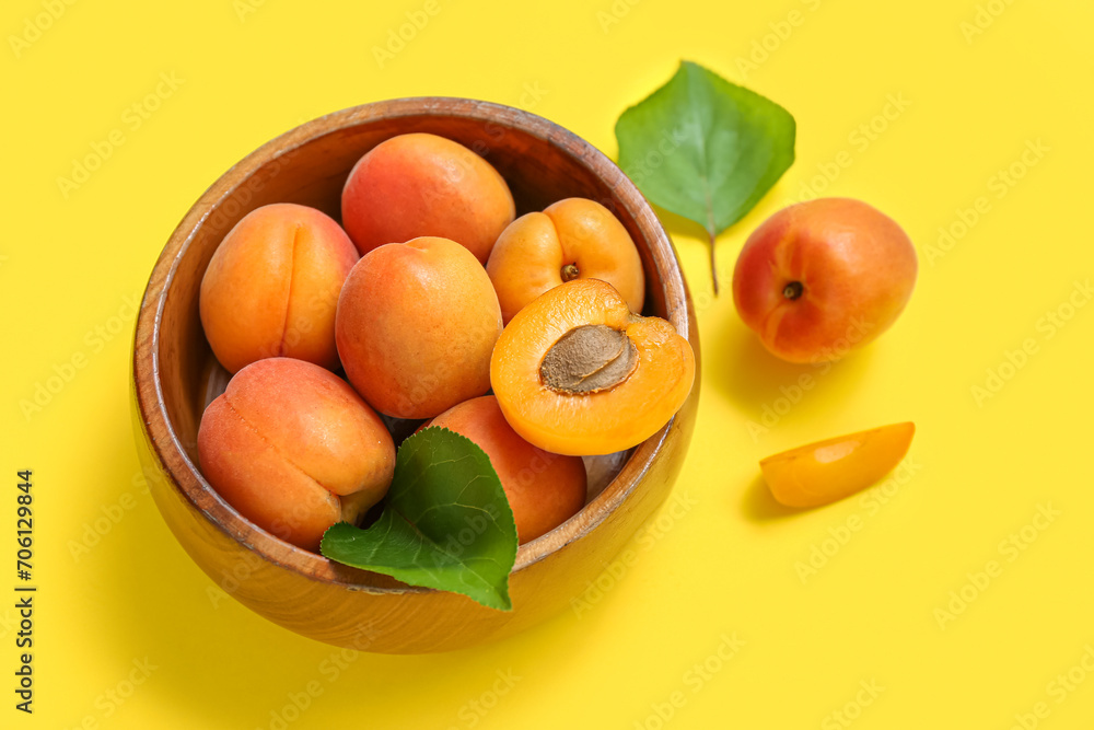 Bowl with fresh apricots and leaves on yellow background