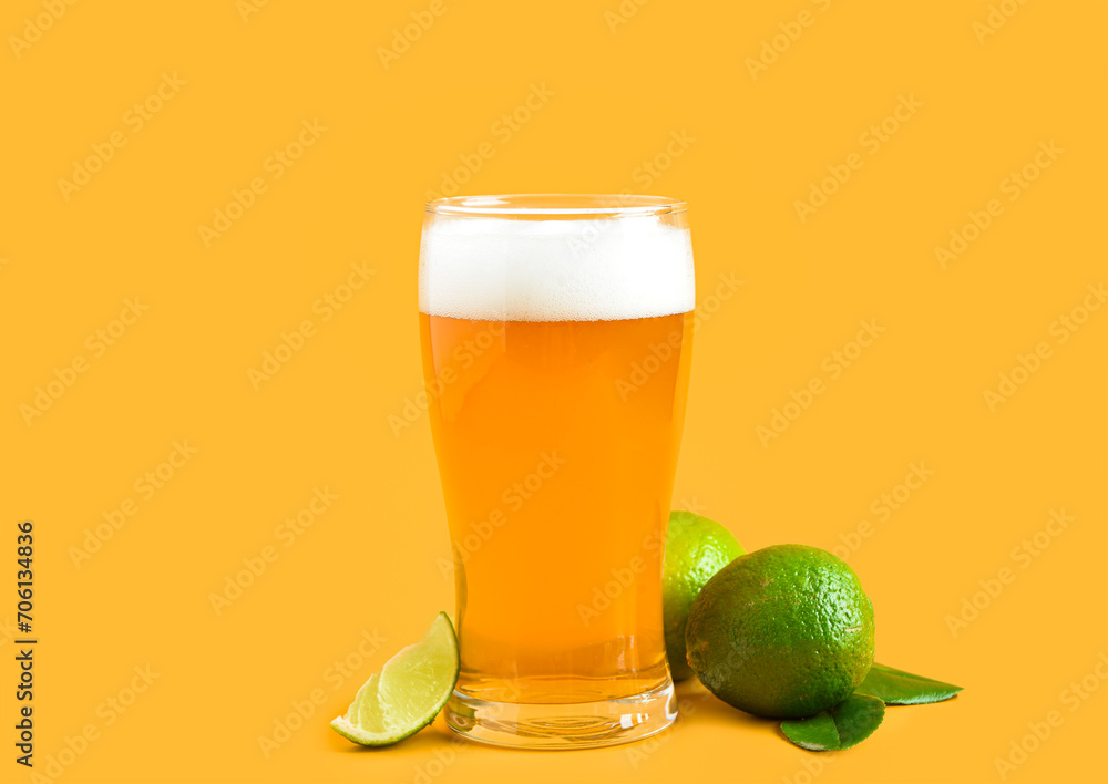 Glass of cold beer with lime on yellow background