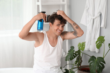 Canvas Print - Handsome young man with tattoo applying hair spray on his curly hair in bathroom