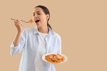 Poster - Young woman eating tasty pasta on beige background